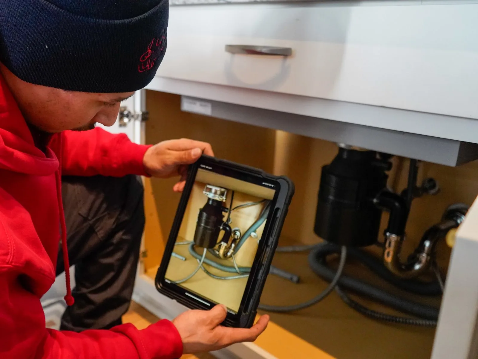 J. Blanton plumber showing a tablet photo of the garbage disposal installed under a kitchen sink