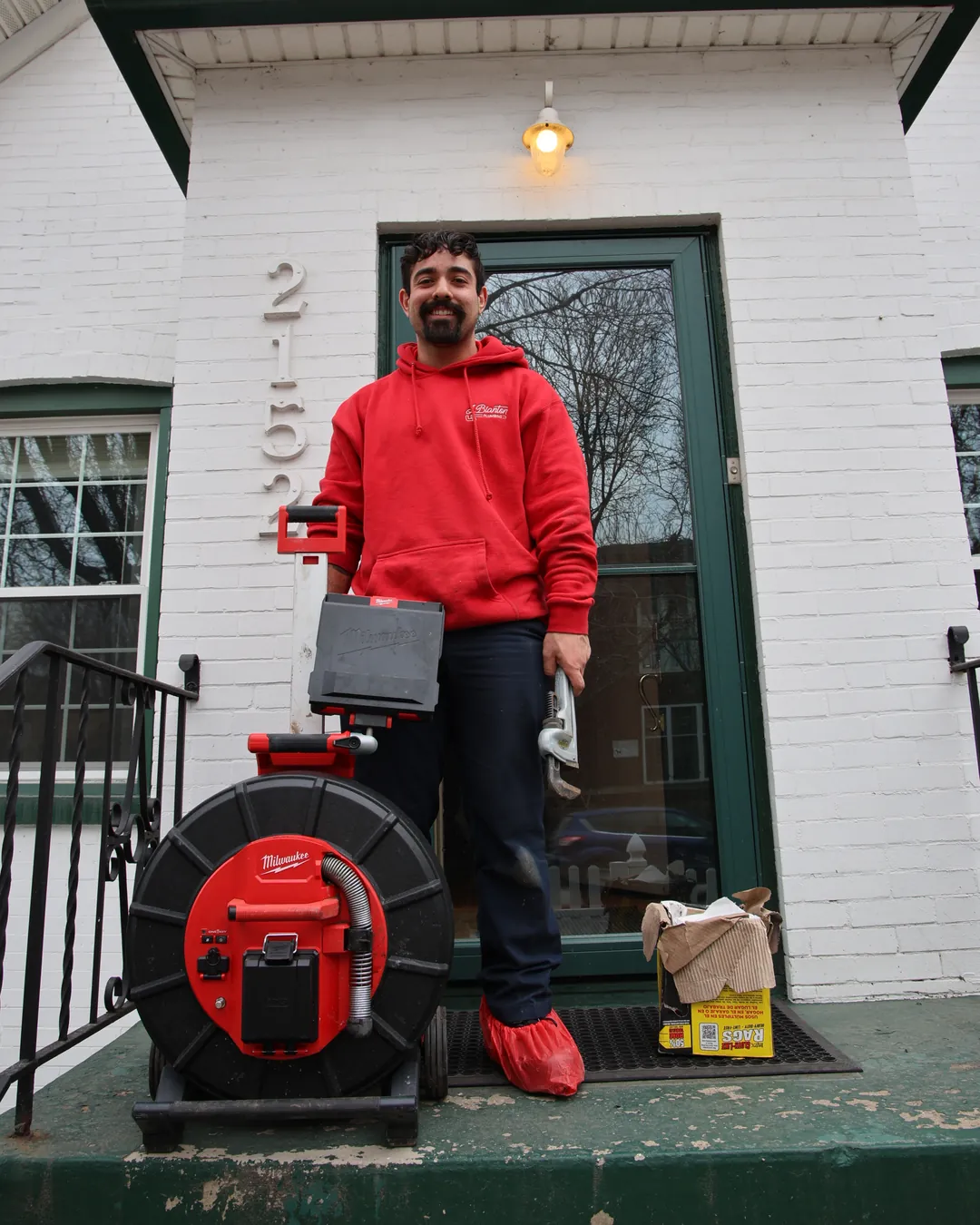 J. Blanton plumber in shoe covers on a home’s front steps with a sewer camera