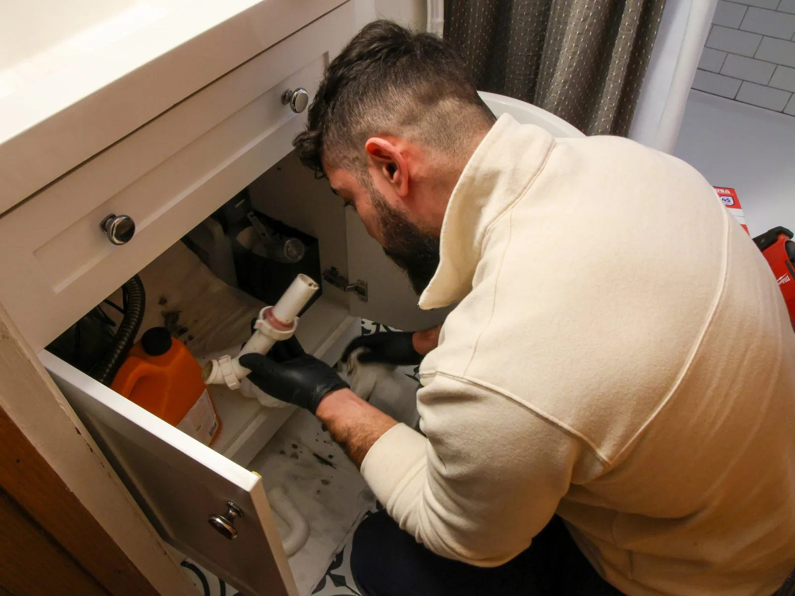 Plumber checking the drain and supply lines under a bathroom vanity during routine maintenance