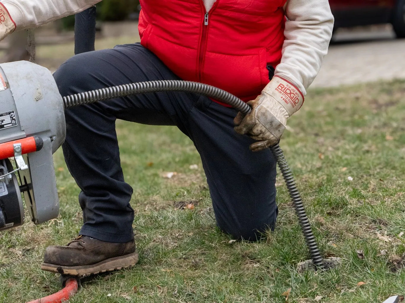 J. Blanton plumber feeding the cable from a drum rodding machine into an outdoor sewer cleanout in a front yard