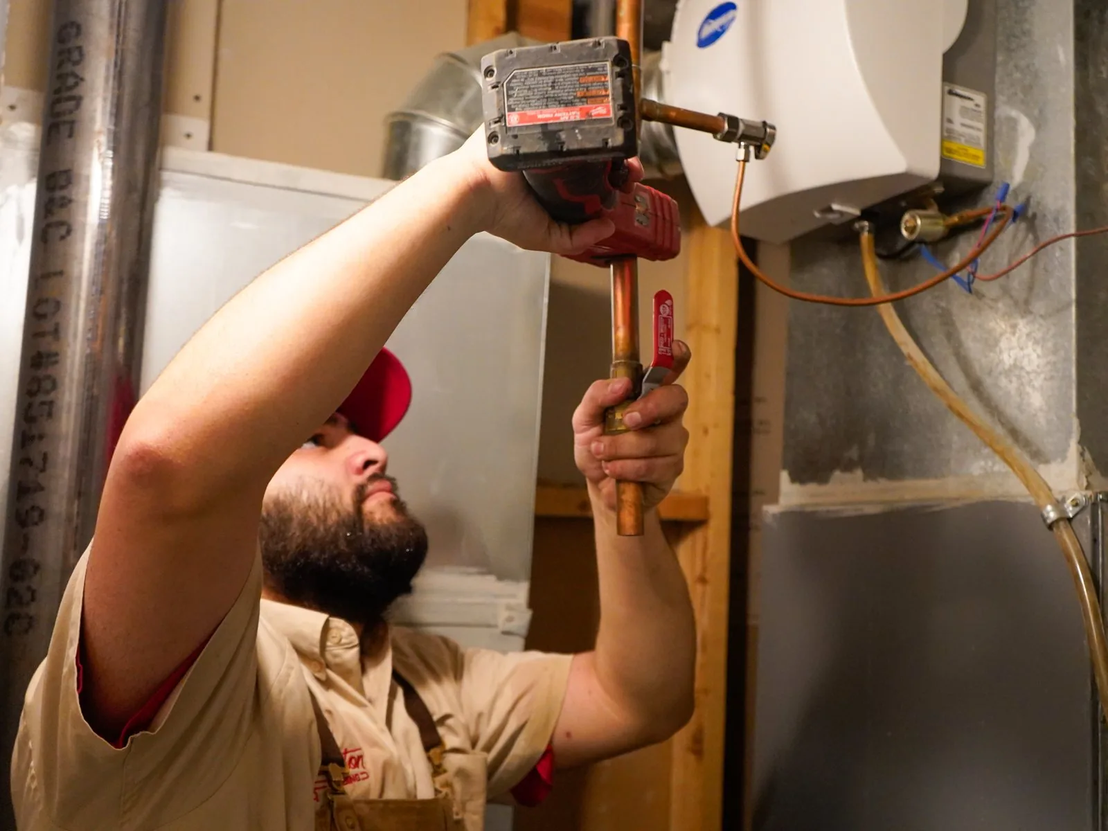 Plumber working on the copper water lines of a wall-mounted tankless water heater in a basement