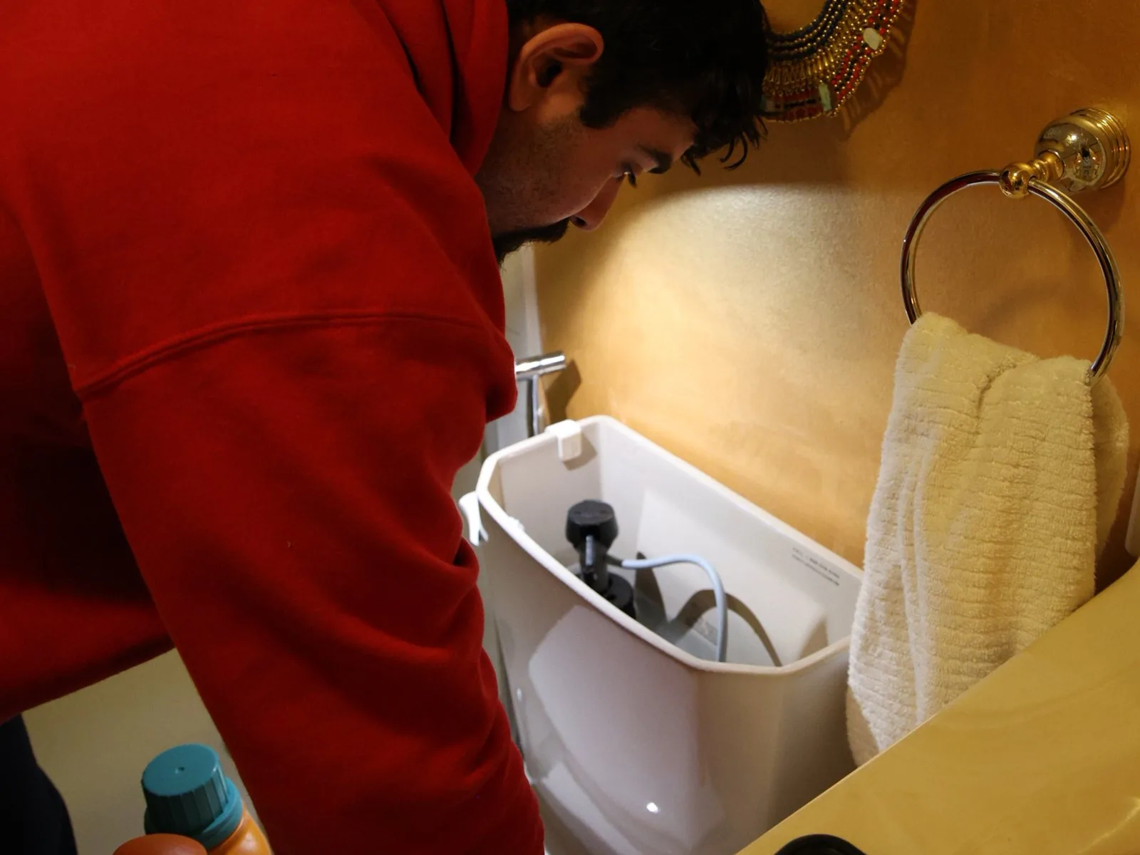 J. Blanton plumber leaning over an open toilet tank to check the fill valve during a toilet repair