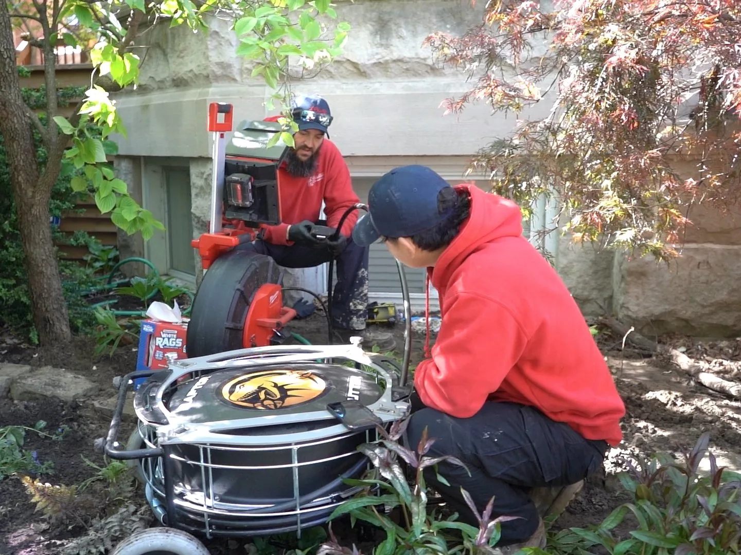Two J. Blanton plumbers setting up sewer camera and cable equipment beside a home's foundation before a trenchless sewer repair