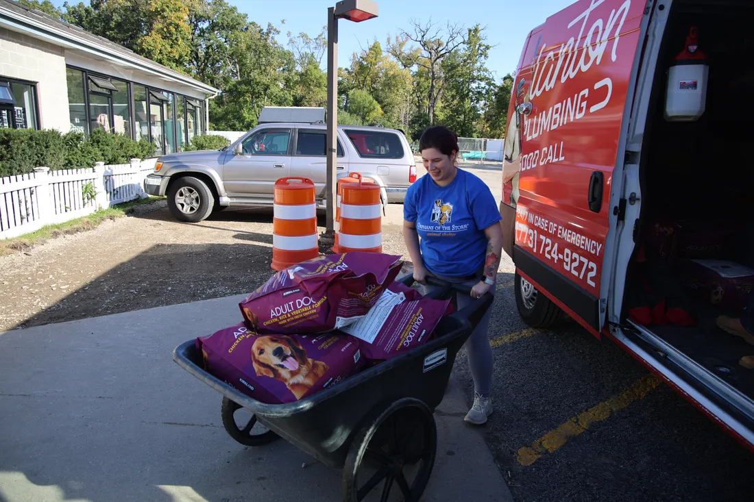 Orphans of the Storm staff member wheeling a cart of donated dog food past the J. Blanton Plumbing van