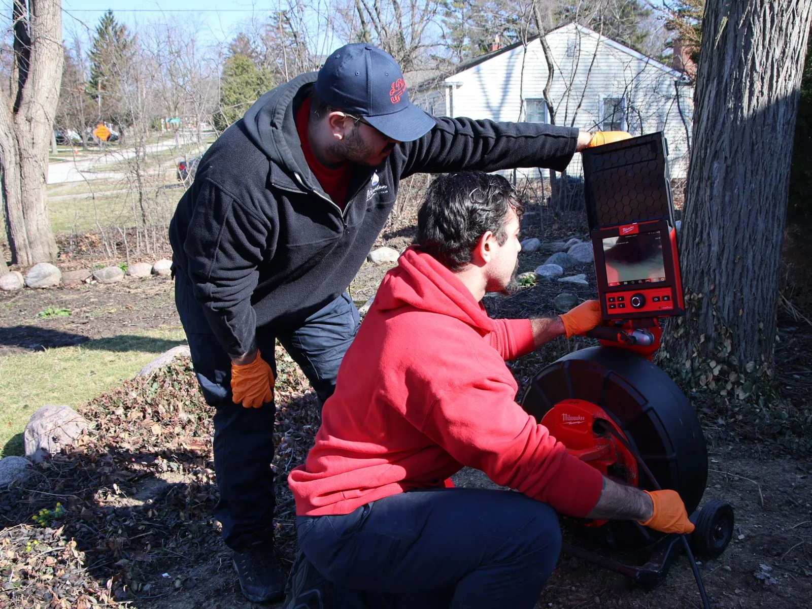 Two J. Blanton plumbers watching the monitor of a sewer camera during a backyard sewer line inspection