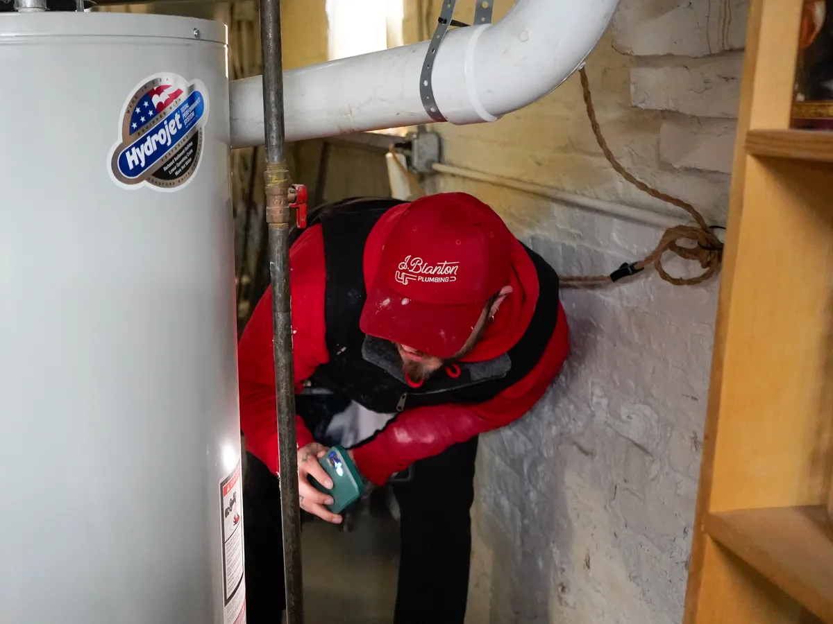 J. Blanton Plumbing technician inspecting a tank water heater in a basement